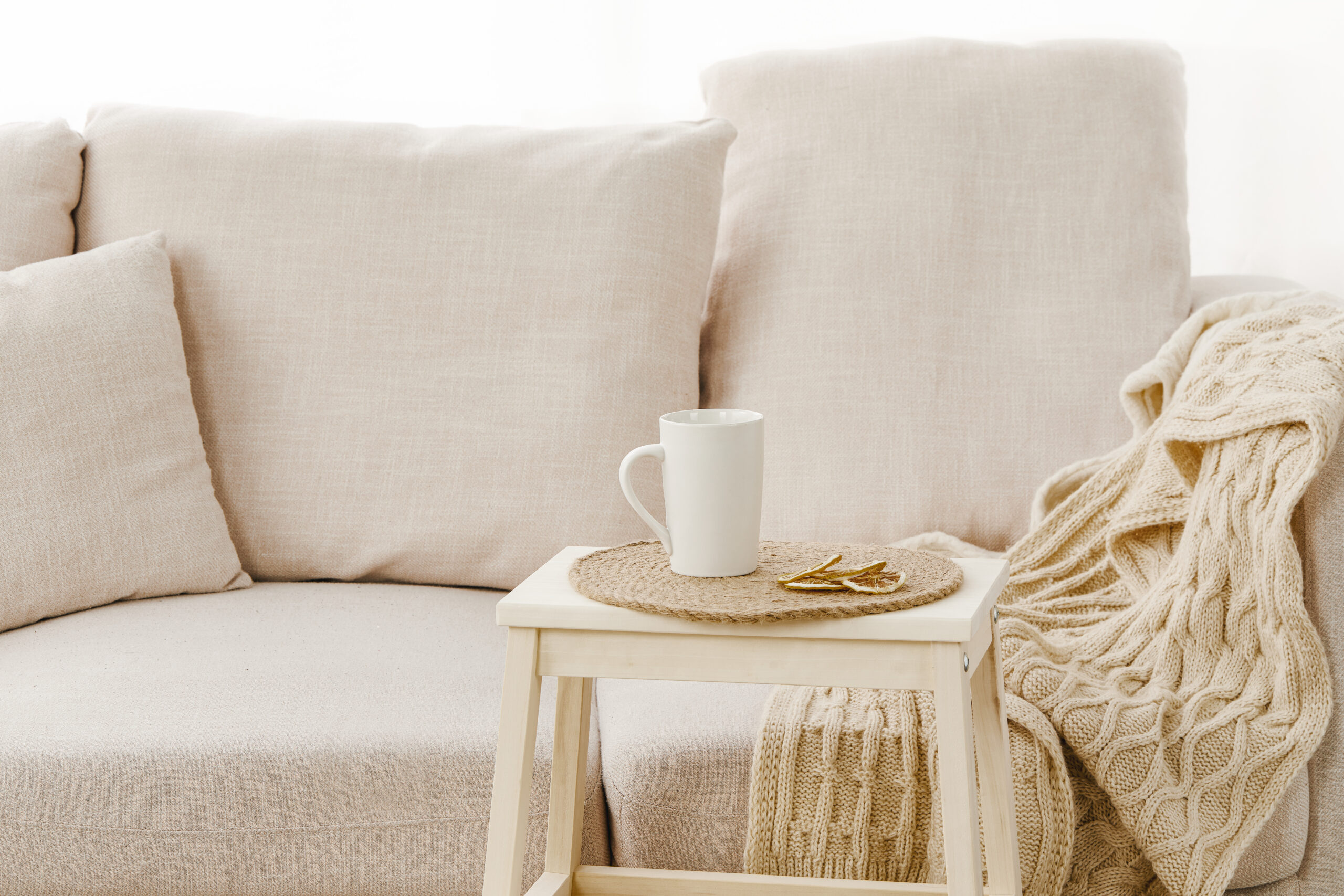 A closeup of a small table with a mug on it near a beige sofa under the lights